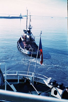 Mid-20th century tugboat "Flugger 17" from Hamburg, flying German flag, navigating port waters. Industrial harbor infrastruct...