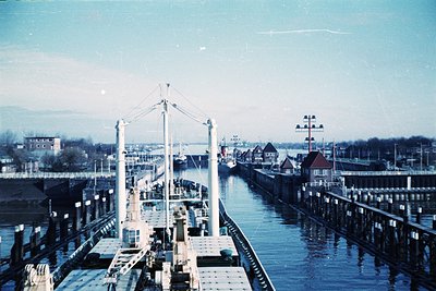Vintage aerial view of a canal with industrial docks, likely mid-20th century. Steel cranes and loading platforms line both s...