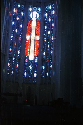Vibrant stained-glass window featuring geometric patterns in red, blue, and white. Central vertical stripe mimics a flag’s de...