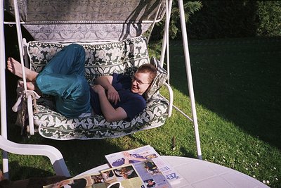Vintage swing chair with floral-patterned cushion, mid-20th century style. Two individuals lounging outdoors, one reading a m...
