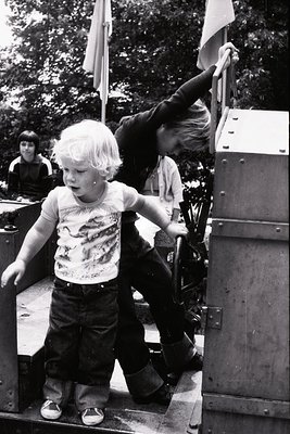 Mid-20th century black-and-white photo: two children climbing a military-style vehicle, likely a jeep or armored car, with a ...