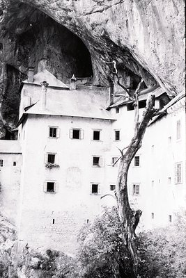 Historic cliffside fortress with steeply pitched roofs and narrow windows, perched on a rocky outcrop. Architectural style su...
