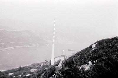Mid-20th century coastal radio tower on cliffside overlooking foggy sea. Distinctive white-and-black striped antenna against ...