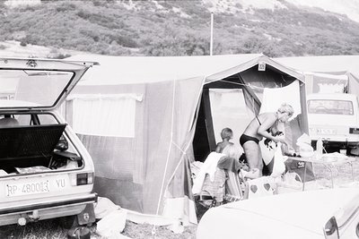 Vintage camping scene with a Yugo car (YU license plate) and canvas tent. Two adults and a child prepare food near an open tr...