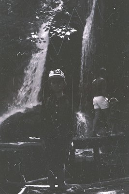 Black-and-white photo of two workers in industrial gear operating a large, cascading water system, likely a cooling tower or ...