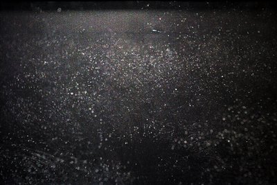 High-contrast nighttime urban scene with dense light pollution. Glowing streetlights and reflections create a textured, abstr...