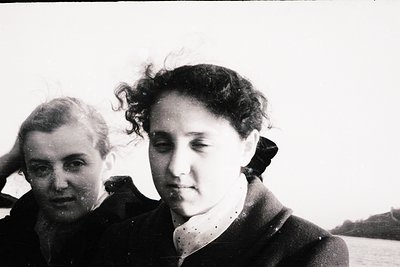 Black-and-white portrait of two women in close proximity, likely mid-20th century. The woman in focus wears a dark jacket wit...