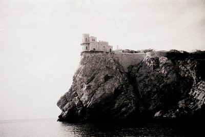 Historic coastal fortress perched on jagged cliffs overlooking the sea. Monolithic stone structure with square tower and cren...