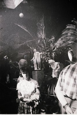 Vintage black-and-white interior shot featuring a woman in a 1950s-style dress holding a small child, surrounded by ornate pa...