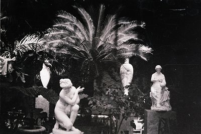 Classic black-and-white interior featuring three classical sculptures: a seated cherubic figure, a standing draped female, an...