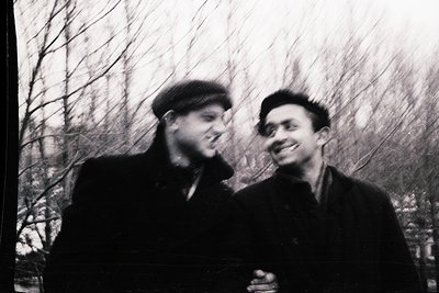 Black-and-white portrait of two men in winter forest, mid-20th century. Both wear flat caps and heavy coats, suggesting cold ...