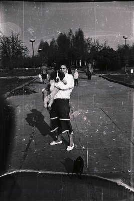 Vintage black-and-white photo of a man holding a child in an outdoor pool area, likely from the 1960s–70s. Concrete pool with...