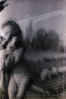 Vintage sepia-toned photo of a seated child in a park, blurred but showing a light-colored dress and dark hair. Distant trees...