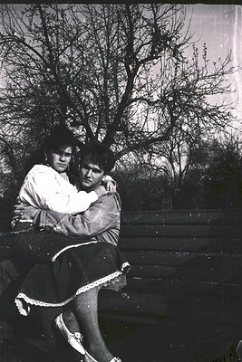 Two individuals embrace outdoors in a mid-20th-century black-and-white photo, likely . One wears a light blouse with lace tri...