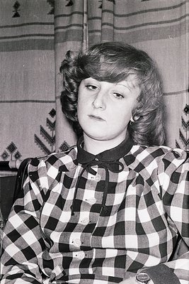 Portrait of a young woman in a plaid blouse, likely from the 1950s–1960s. Her hairstyle features a side-parted bob with soft ...