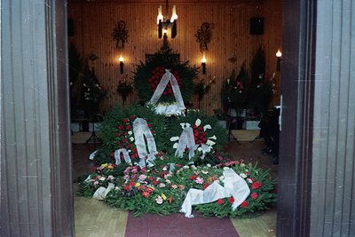 Vintage funeral memorial arrangement featuring three draped caskets surrounded by floral tributes in a dimly lit indoor setti...