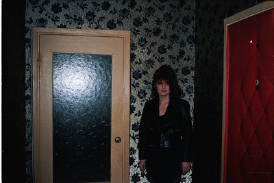 Vintage interior shot featuring a woman in a dark doorway flanked by floral wallpaper and a red-patterned door. Mid-century s...