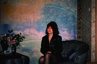 Vintage portrait of a woman seated in a dimly lit interior, framed by a mural depicting a serene landscape with trees and wat...