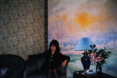 Vintage interior portrait featuring a person seated in a dark, textured armchair against a wall adorned with an impressionist...