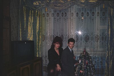 Vintage indoor portrait featuring two individuals in formal attire—woman in a black dress, man in a suit—posing beside a deco...