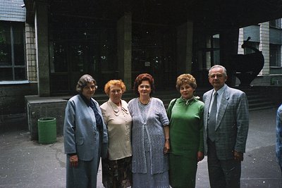 Five individuals pose outdoors in matching formal attire—women in knee-length dresses (1960s-70s styles) and a man in a tweed...