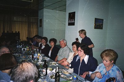 Mid-20th century gathering in a formal dining hall, likely . Long table set with wine bottles, glasses, and plates. Attendees...