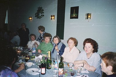 Vintage indoor gathering in a dimly lit dining hall, featuring a group of adults seated around a long table laden with wine b...