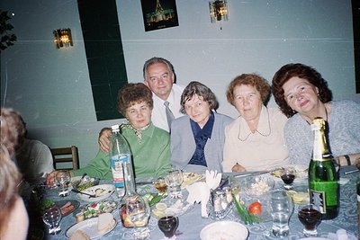Vintage group portrait at a formal dinner, likely Eastern European . Five adults pose at a long table adorned with plates, cu...