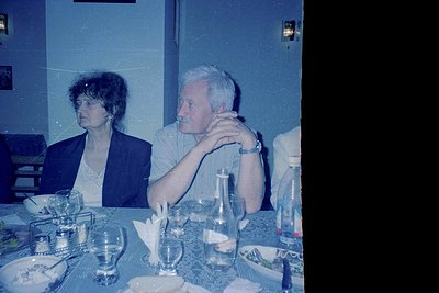 Vintage indoor portrait of two adults seated at a formal dining table, likely mid-20th century. The man wears a watch and a d...