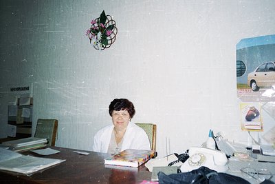 Vintage office interior featuring a woman seated at a wooden desk with analog phone, vintage calendar (2001), and framed post...