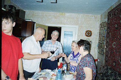 Vintage indoor gathering featuring four adults and a teen in a modestly decorated living/dining space. A man in a checkered s...