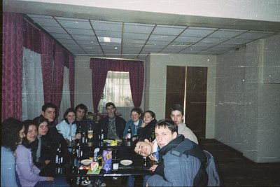 Vintage group photo in a dimly lit indoor setting, likely a 1990s-era restaurant or lounge. Nine individuals seated around a ...