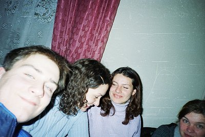 Vintage group selfie in dim indoor lighting, likely 1990s–2000s. Four individuals pose closely in a room with plain walls and...