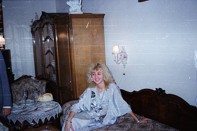Vintage interior featuring a woman in a floral-patterned robe seated on a tufted sofa in a mid-century living space. Wooden a...