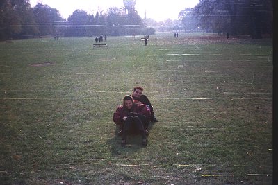 Vintage photo of two individuals sitting on grass in a park, likely mid-20th century. The scene captures a relaxed moment wit...
