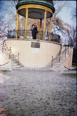 Neoclassical pavilion with yellow columns and black wrought-iron railings, featuring a circular observation deck. Two figures...