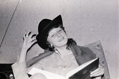 Vintage black-and-white portrait of a person in a fedora and plaid shirt, holding an open book with a vintage radio or tape r...