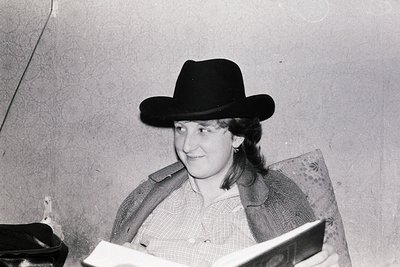 Black-and-white portrait of a person wearing a wide-brimmed cowboy hat indoors, seated while reading. Mid-century styling wit...