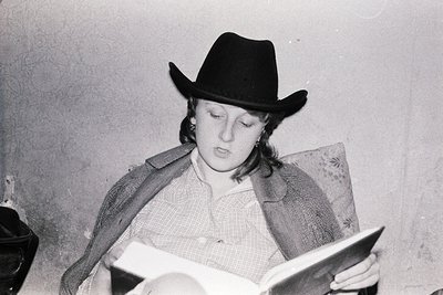 Black-and-white portrait of a person in a cowboy hat reading an open book indoors, likely mid-20th century. Plain wall and mi...