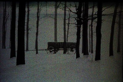 Monochromatic image showing a weathered wagon situated within a dense, leafless forest. Heavy snowfall blankets the ground, o...
