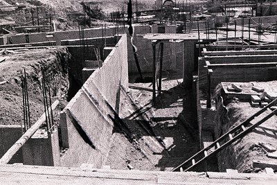 Black and white photo depicts the construction of a reinforced concrete structure, possibly a dam or retaining wall. Visible ...
