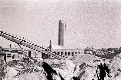 Industrial landscape view; a conveyor belt dominates the foreground, descending over excavated earth. Background features a m...