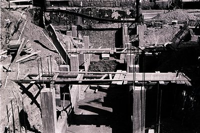 Aerial view captures a building under construction. Visible are reinforced concrete slabs, scaffolding, and formwork. The sit...