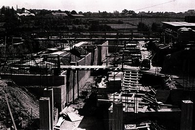 Construction site, likely post-war Europe. Concrete formwork and scaffolding surround a multi-level structure under developme...