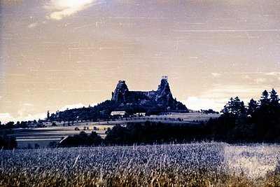 A dramatic, vintage color photograph showcases a hilltop castle overlooking a tiered, agricultural landscape. The castle feat...