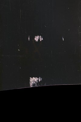 Highly distressed black surface with visible scratches and areas of paint loss revealing a lighter layer beneath. Appears to ...