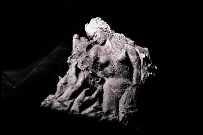 Fragment of a sculpted, reclining figure, possibly female, rendered in a textured, earthen material. The subject appears drap...