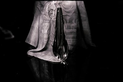 Elegant black glass vase rests on a draped fabric, reflecting in a glossy surface. The composition emphasizes form and shadow...