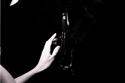Monochrome image showing a hand holding a tall, elegant glass vase against a dark background. The vase’s form is elongated, w...