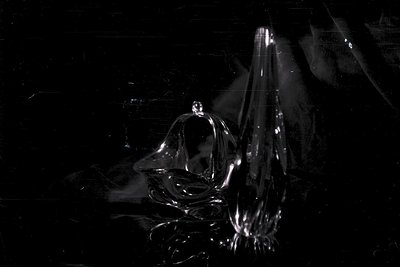 Elegant, clear glass sculpture or vase rests on a black, textured surface. Minimalist composition with sharp reflections high...